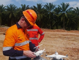 Man in high viz clothing and safety helmet looking at a drone he is holding